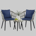 A grey 3-piece PE rattan outdoor bistro set with two padded chairs and a tempered glass-top table on a cozy apartment balcony.